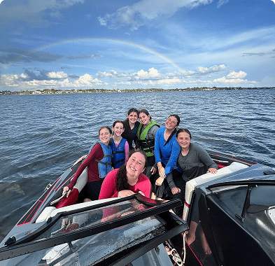 Group of friends smiling on a boat in a scenic lake under a blue sky.
