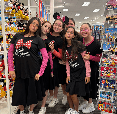 Five friends dressed in coordinated black outfits posing in a toy store aisle.