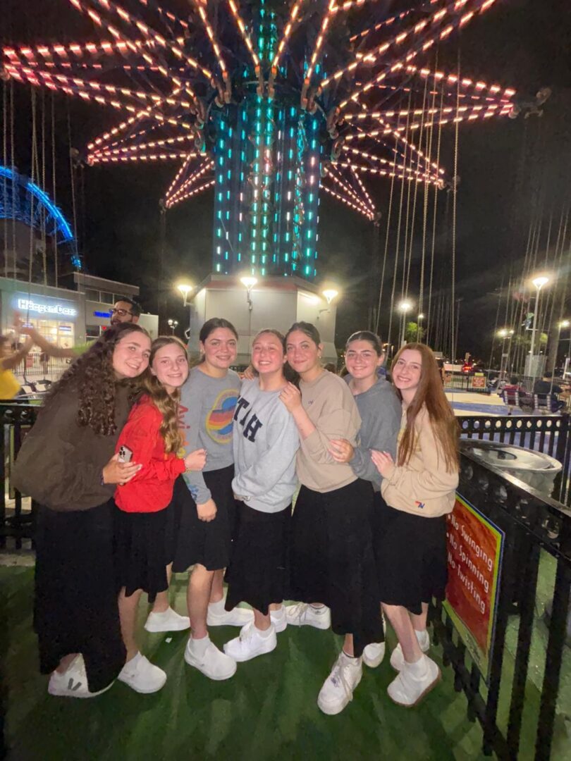 A group of friends smiling together at an amusement park at night.