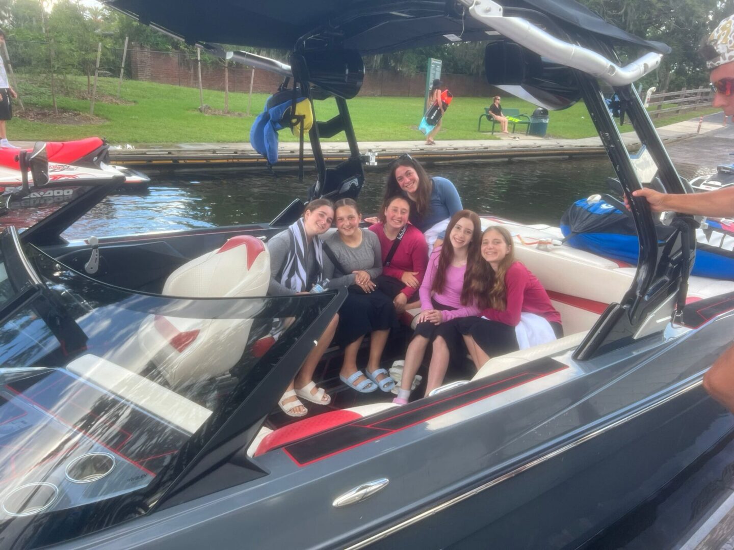 Four friends smiling on a boat in a sunny park setting.