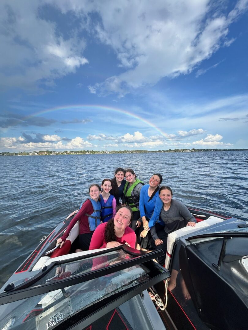 Group of friends enjoying a boat ride on a sunny day with a rainbow in the sky.