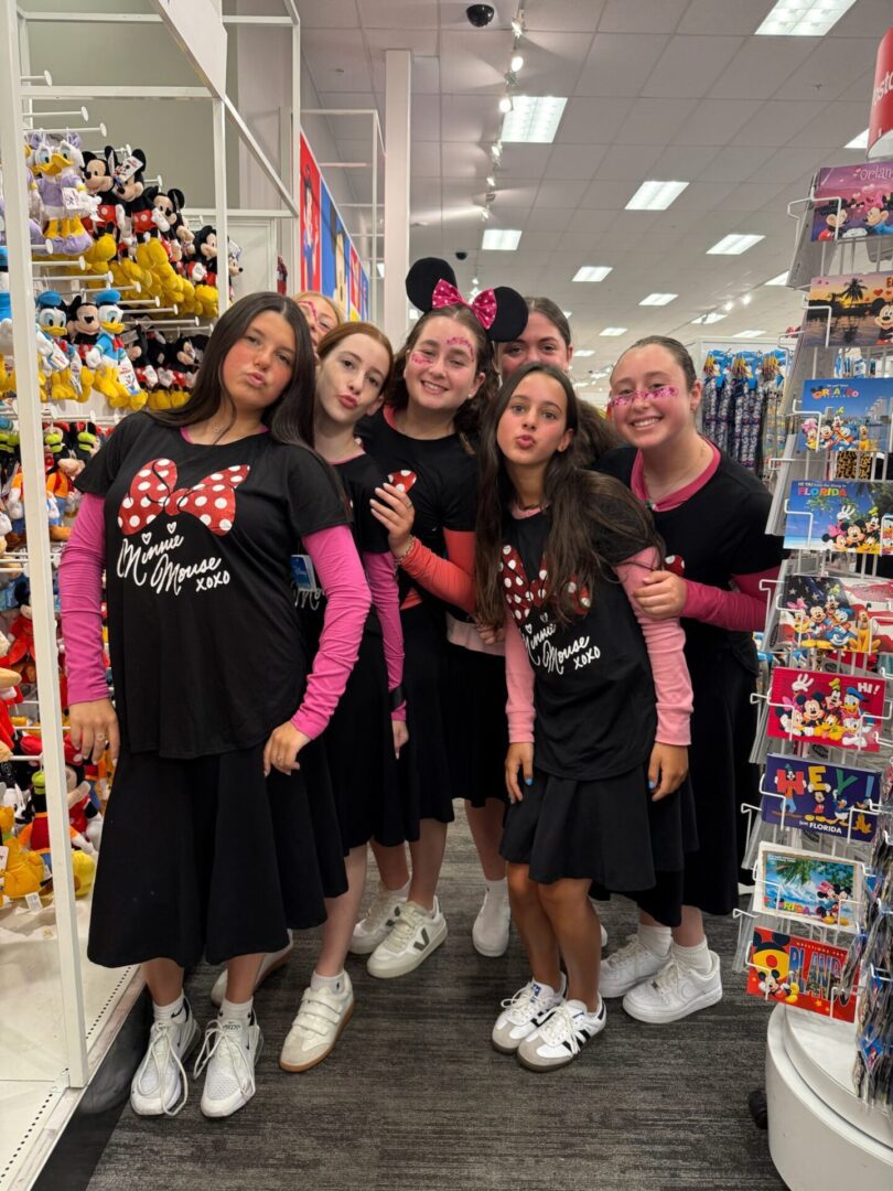 Five girls posing happily in a toy store aisle filled with colorful plush toys.
