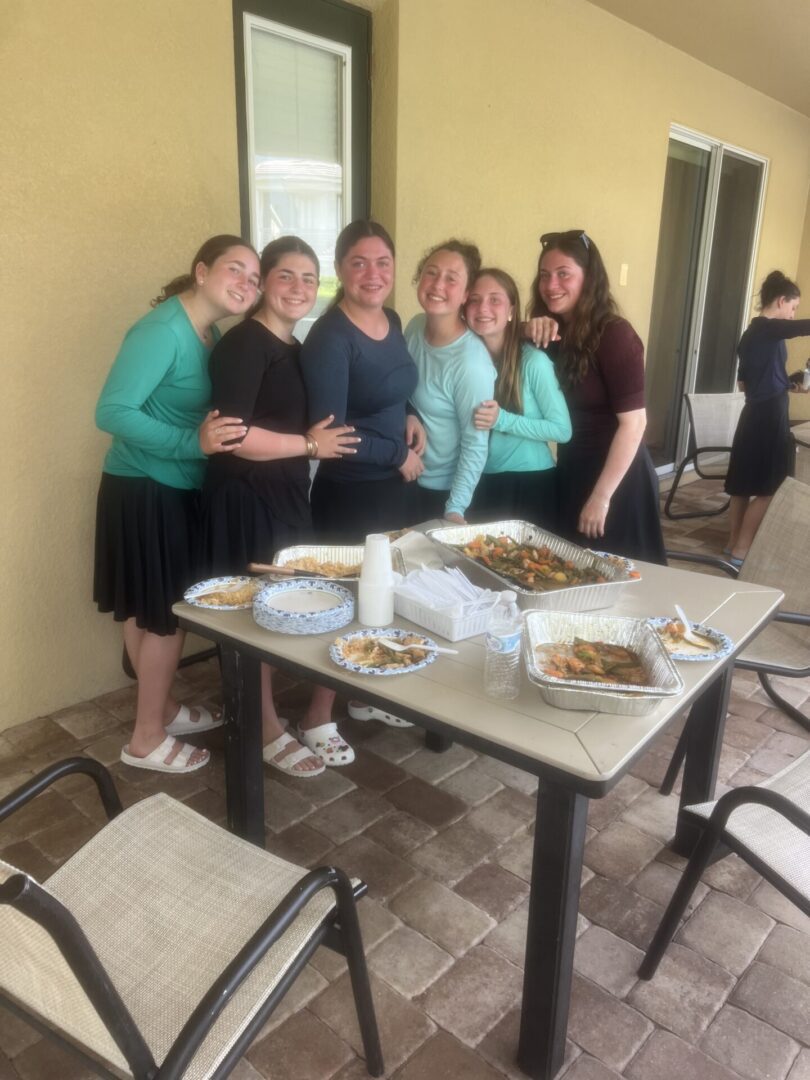 A group of six women standing and smiling near a table with food.
