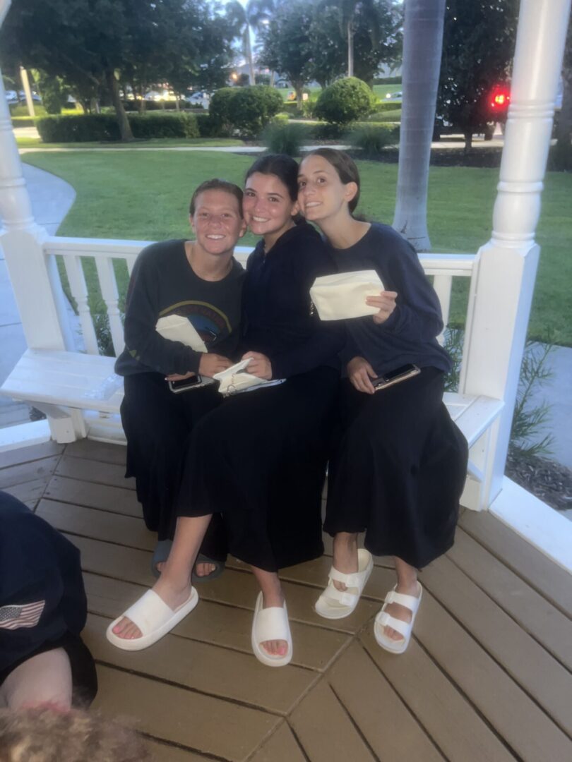 Two women in black dresses sitting on a porch, holding cake slices.