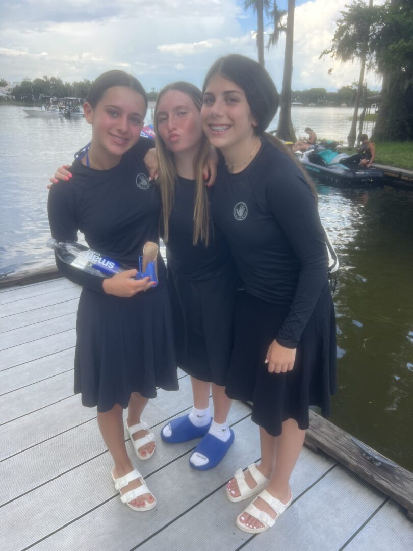 Three girls in matching black dresses posing by a lakeside dock.