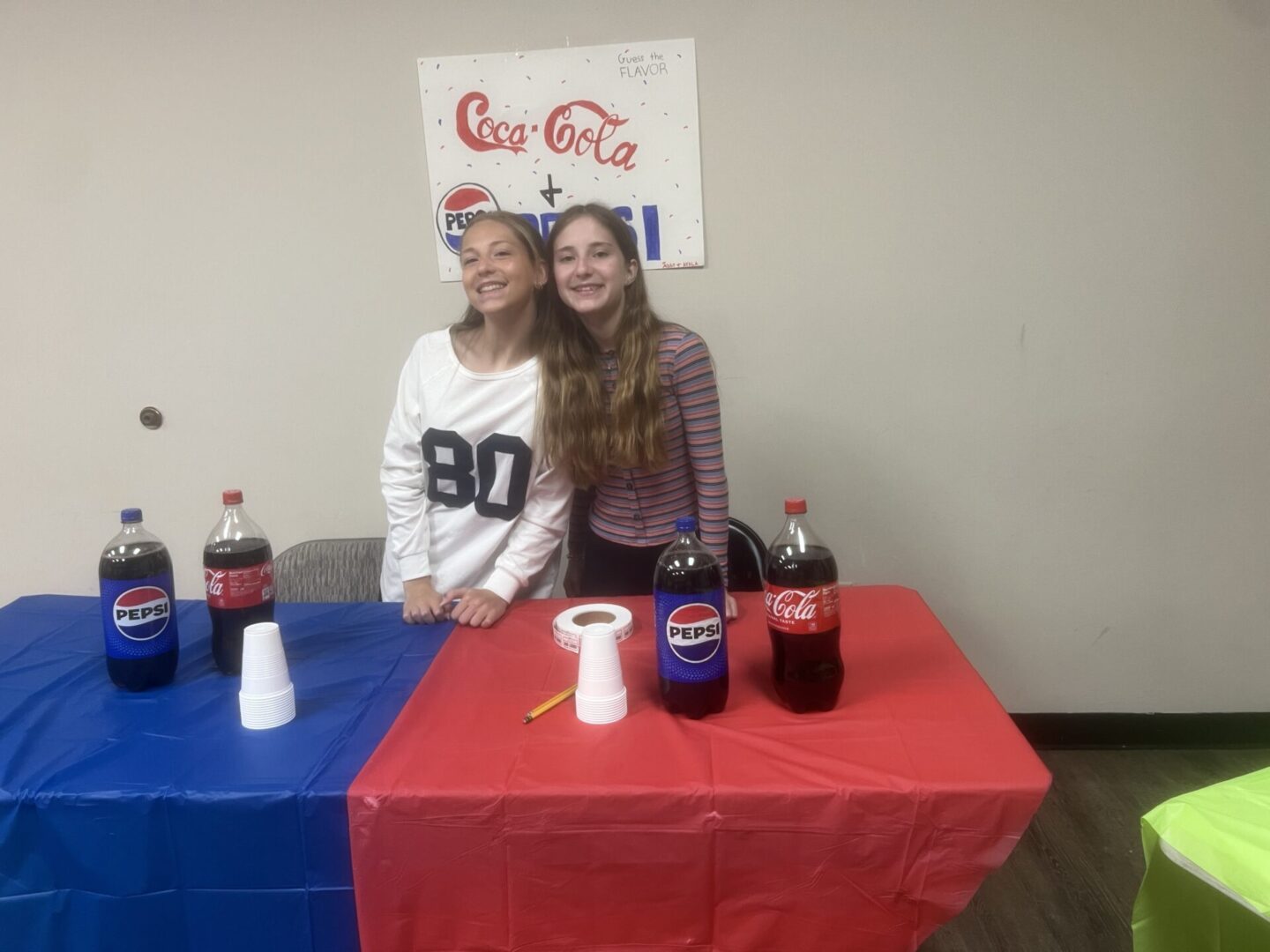 Two young women standing behind a table with Coca-Cola and Pepsi bottles.