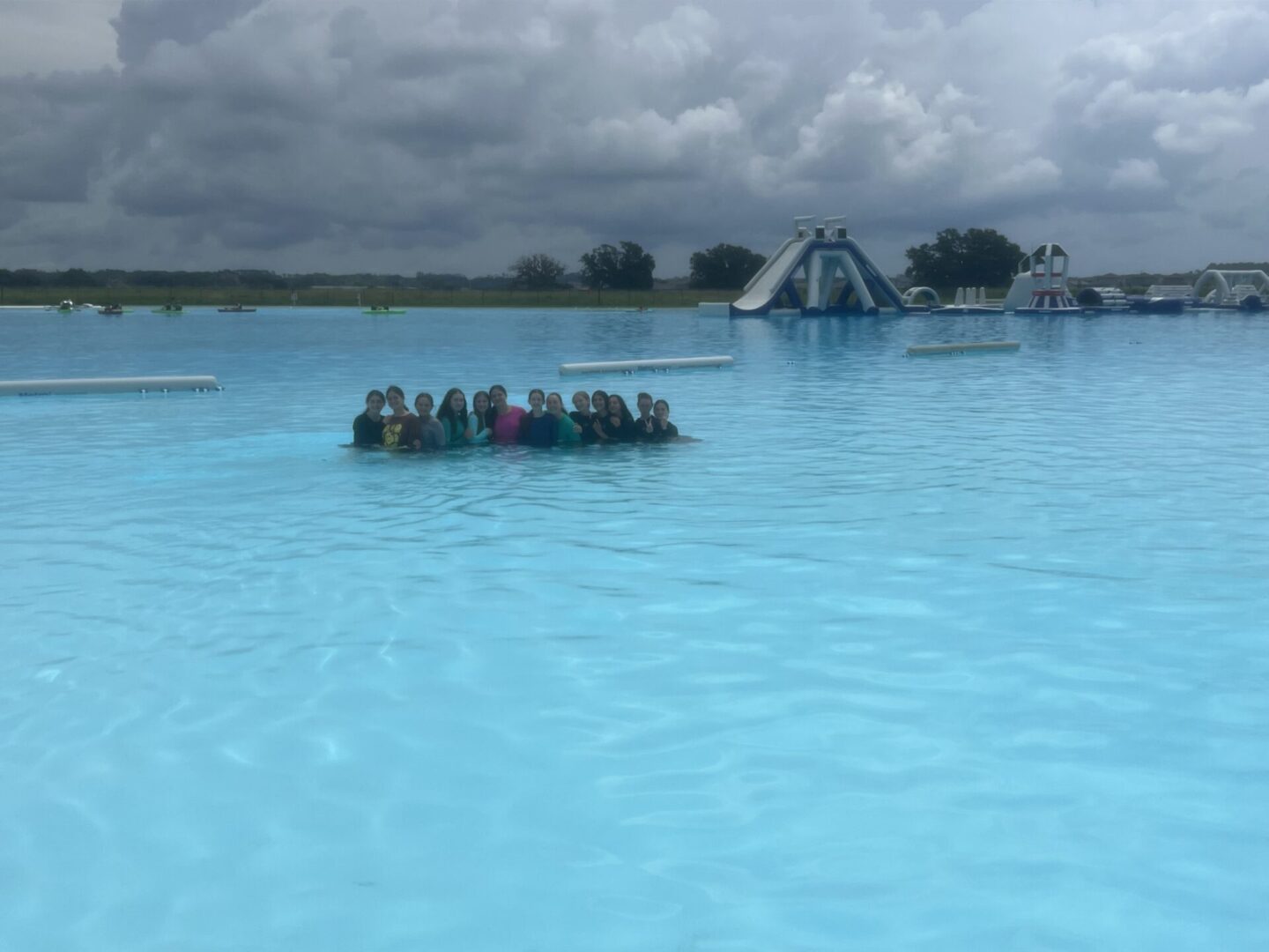 Group of people gathered on a floating platform in a large pool under cloudy skies.