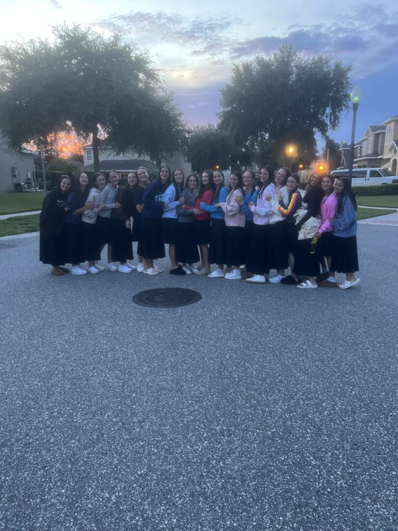 Group of young women posing outdoors in casual outfits during dusk.