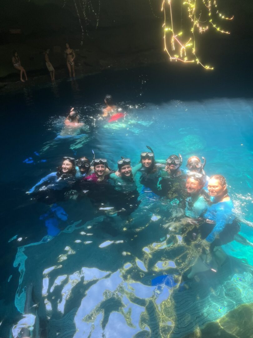 Group of snorkelers posing in clear blue water inside a cave.