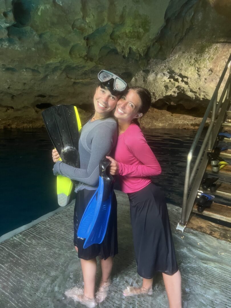 Two women posing happily near water and stairs in a cave setting.