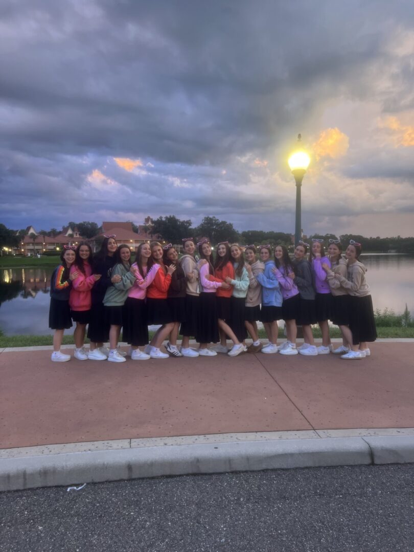 Group of friends posing by a lakeside at dusk with street lamps lit.