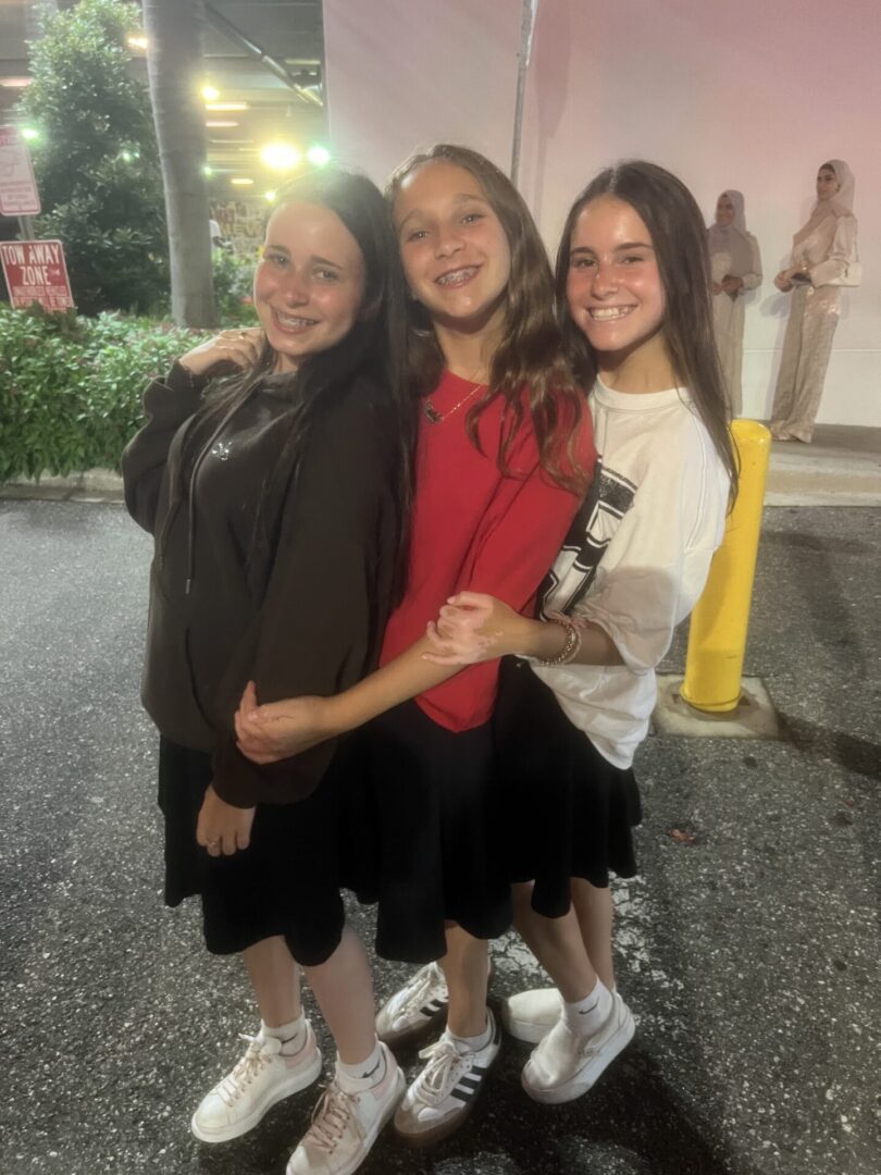 Three young women embracing and smiling outdoors at night.