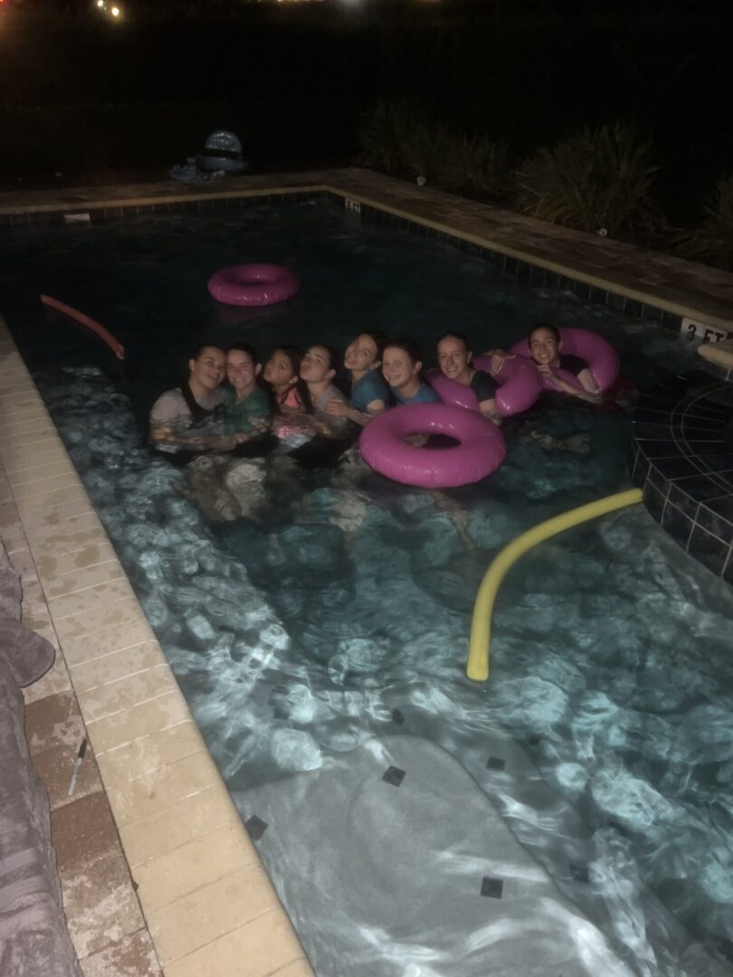 Group of people enjoying a nighttime swim with pool floats.