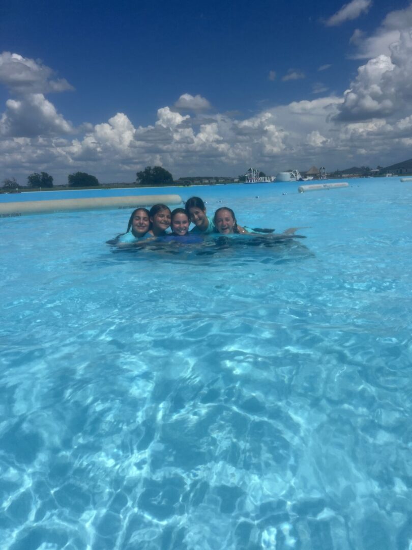 A group of friends enjoying a swim in a clear blue pool under a sunny sky.