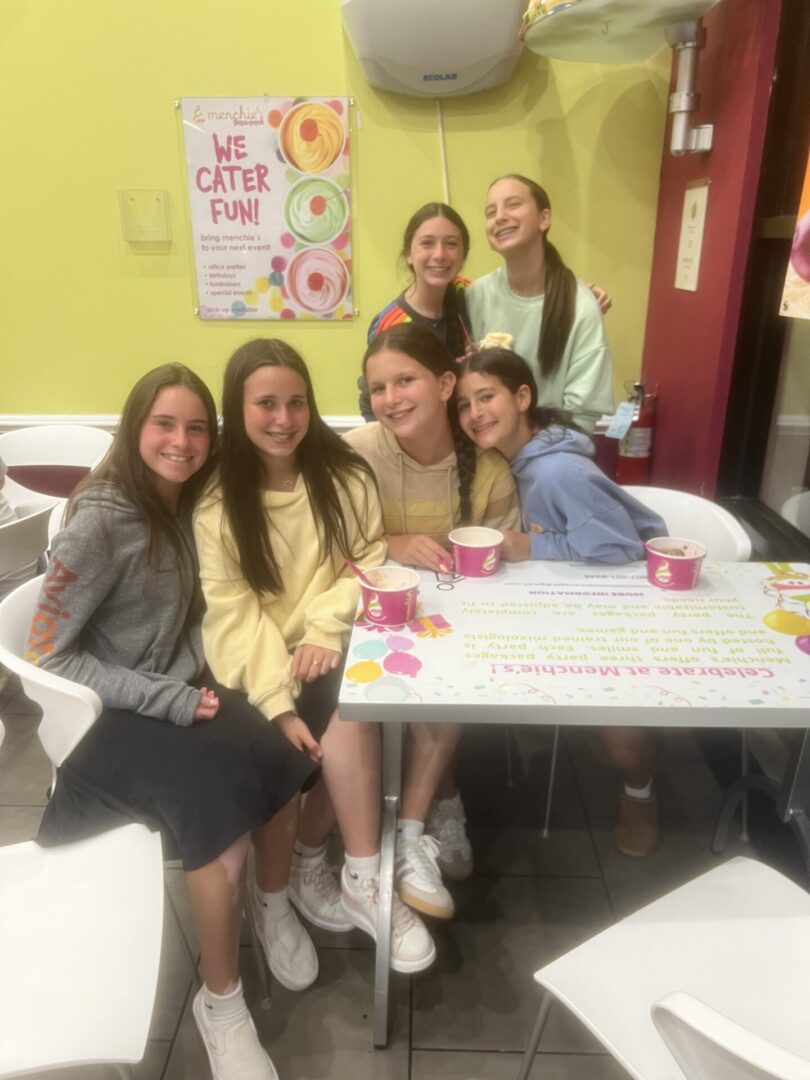 A group of six young women smiling at a table with snacks and drinks.