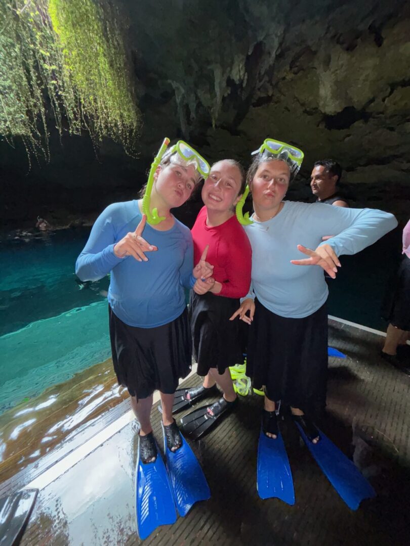 Three people smiling inside a cave near blue water.