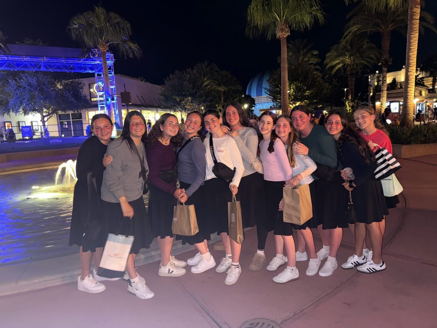 Group of young women posing together outdoors at night, all wearing matching white socks and sneakers.