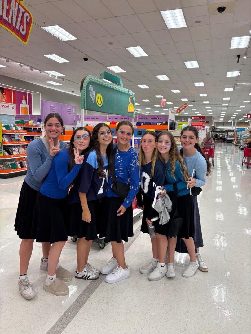 A group of six young women smiling and posing inside a brightly lit store.